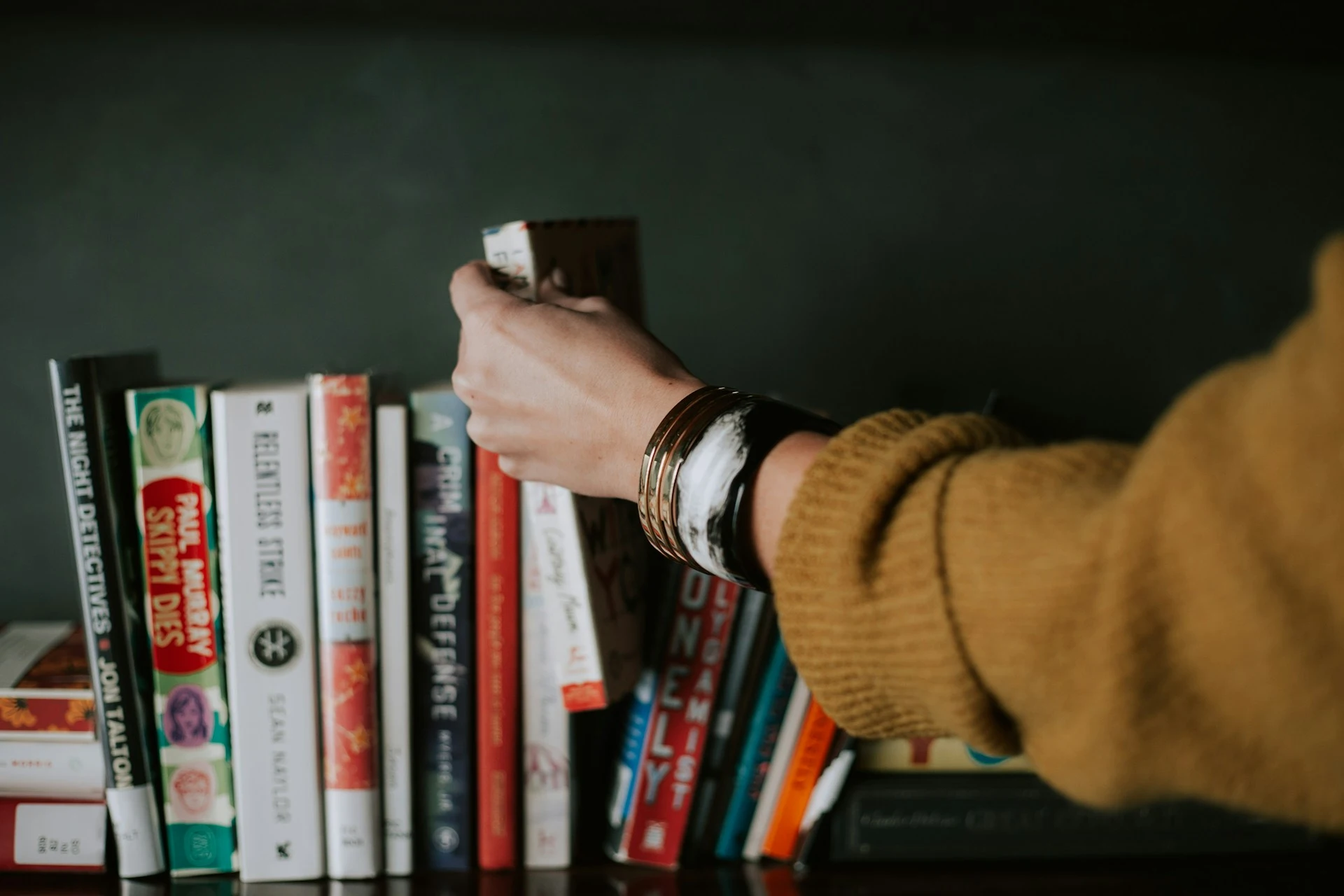 A person picking white and red book on a bookshelf
